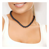 Une femme portant un haut blanc sans manches sourit, mettant en valeur le Perlinea Collier NOELYSE en argent avec perles noires de 9/10 mm et mousqueton fermoir autour de son cou. L'accent est mis sur le collier, le cou et le bas du visage.