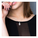 Une femme vêtue d'un haut noir avec un panneau transparent porte le collier Beloved Collier "FOREVER SWAROVSKI", souriant en touchant ses lèvres, révélant d'élégants ongles noirs et un pendentif étincelant.