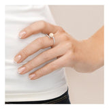 Gros plan sur une main à la manucure française portant la Bague ZIGZAG de Perlinea en or blanc et perle de culture rose, reposant sur un fond clair. La personne porte un haut blanc et un jean foncé pour un style raffiné d'inspiration française.