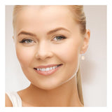 Une femme souriante aux cheveux blonds et aux yeux clairs porte les Boucles d'Oreilles DIANA | Argent & Perles de Culture Roses de Perlinea. Elle fait face à l'appareil photo avec un maquillage naturel sur un fond uni et clair.