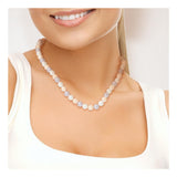 Une femme vêtue d'un haut blanc sans manches porte le collier Perlinea Collier NOELYSE - un collier de perles multicolores de 8/9 mm avec un fermoir jaune. Son cou et son collier sont mis en évidence, tandis que son visage est partiellement visible alors qu'elle sourit doucement.