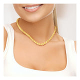 Une femme vêtue d'un haut blanc sans manches sourit, dévoilant ses dents, tout en portant le Collier NOELYSE | Or Jaune & Perles Dorées de Perlinea. L'image recadrée met en évidence son cou, sa clavicule et le bas de son visage.