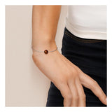 Gros plan sur un poignet orné du Bracelet Argent & Perle de Culture Chocolat - 8/9mm de Perlinea, composé d'une seule perle de culture ronde au chocolat, porté avec un haut blanc et un pantalon noir sur un fond neutre.