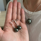 Collier et boucles d'oreilles pendantes ornés de perles de Tahiti noires, portés et tenus en main.