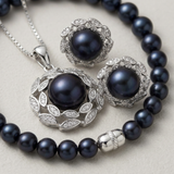 Parure collier, boucles d'oreilles et bracelet perles noires sur fond neutre.