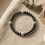 Bracelet perles d'eau douce noires et billes argent 925 sur fond beige naturel.