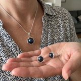 Collier et boucles d'oreilles à perles noires de Tahiti sur monture fleurie argentée, portés et tenus en main.