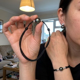 Parure Tahiti portée : collier et bracelet en main, boucle d'oreille perle noire à l'oreille.